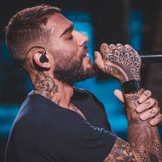 a man with tattoos on his arms holding a microphone to his ear and looking into the distance