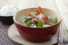 a red bowl filled with food on top of a table next to chopsticks