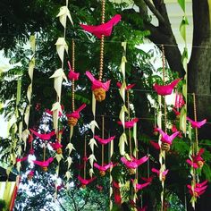 pink and white paper birds hanging from strings in front of a tree with lots of green leaves