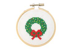 a cross - stitch christmas wreath with a red bow hanging from it's hoop