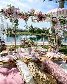 a table set up with pink flowers and candles for a tea party by the water