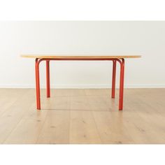 a wooden table with orange legs on a hard wood flooring area in front of a white wall