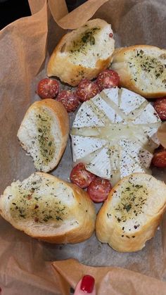 some bread with cheese and tomatoes on it sitting on top of brown wrapping paper next to a woman's hand