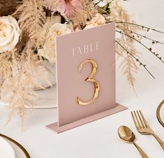 the table numbers are gold on pink and white place cards, with flowers in the background