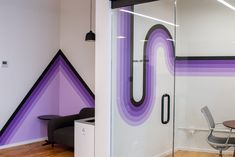 an office with purple and black decor on the wall, glass door to another room