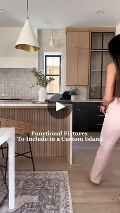 a woman in pink pants walking through a kitchen with an island and dining room table