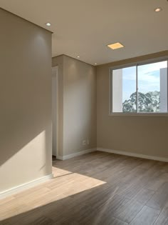 an empty room with hard wood flooring and large windows in the corner, looking out onto trees