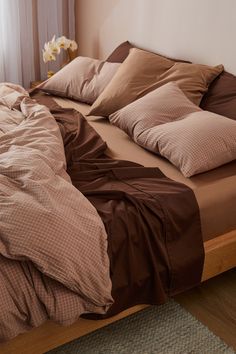 a bed with brown linens and blue pillows in front of a window, next to a wicker basket