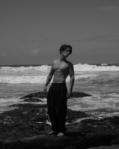 a man standing on top of a rocky beach next to the ocean in black and white