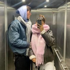 a man and woman standing in an elevator looking at their cell phones while wearing scarves