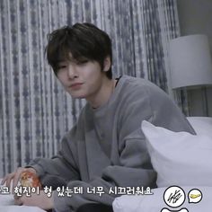 a young man sitting on top of a bed next to a white pillow covered in pillows