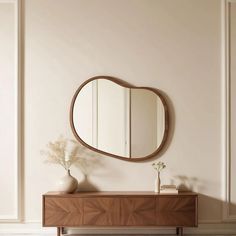 a mirror on the wall above a dresser with vases and flowers in front of it