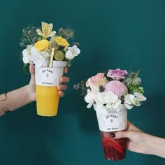 two people holding cups with flowers and drinks in them, one is yellow and the other is red