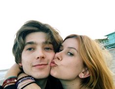 a young man and woman kissing each other on the beach with buildings in the background