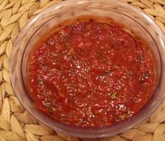 a glass bowl filled with red sauce on top of a woven tablecloth covered basket