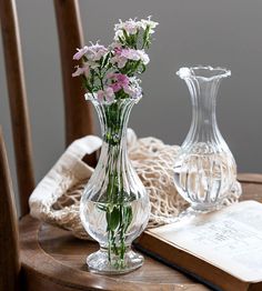 two vases with flowers are sitting on a table next to an open book and lace