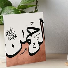 an arabic calligraphy art board on a table with a potted plant in the background