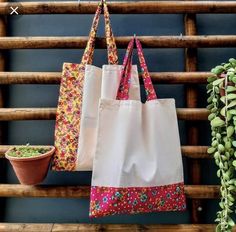 two bags hanging on a wall next to a potted plant and wooden slats