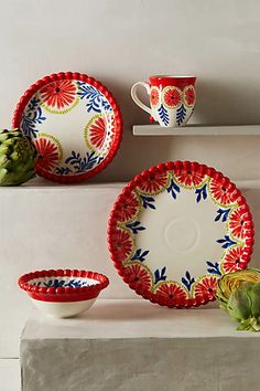 red and white dishes with flowers on them are sitting on a shelf next to succulents