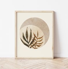 a framed art print with leaves in front of a white wall and wood flooring