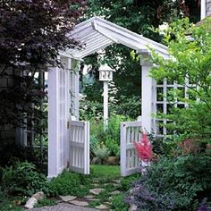 an outdoor garden with white arbors and stone path leading to the entrance area, surrounded by greenery