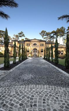 the driveway is lined with trees and cobblestone pavers leading to a large house