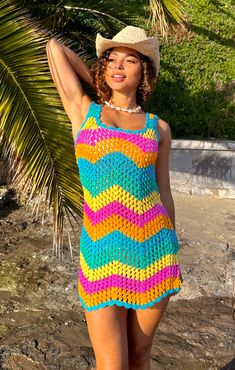 a woman in a colorful crochet dress and hat posing for the camera with her arms behind her head