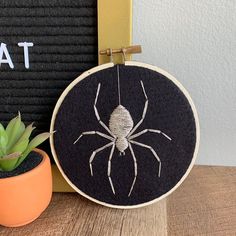 an embroidered spider sits next to a potted succulent