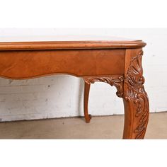 an old wooden table with carvings on the top and bottom, against a white brick wall