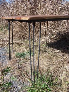 a wooden table sitting in the middle of a dry grass field next to some bushes