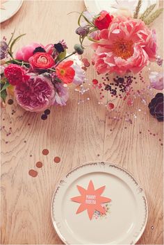 a table topped with plates and flowers on top of a wooden table covered in confetti