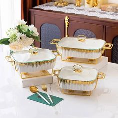 four pieces of white and gold dishes on a table with flowers in vases behind them