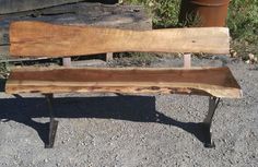 a wooden bench sitting on top of a gravel ground next to a tree trunk and potted plant