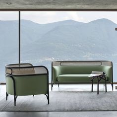 two chairs and a couch in front of a large window with mountains in the background