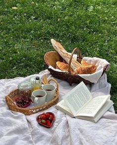 an open book is sitting on a blanket next to a basket full of bread and jams