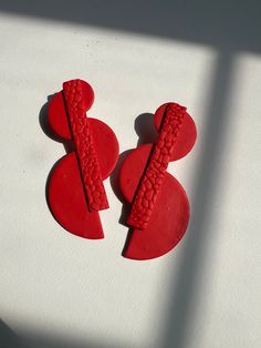 two red ear clips sitting next to each other on a white surface with shadow coming from the back