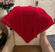 a red crocheted blanket sitting on top of a chair next to a vase with flowers