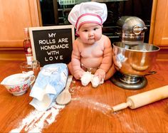 a baby is sitting on the kitchen counter next to some ingredients and a sign that says, my rolls are homemade with love