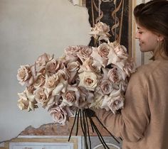 a woman holding a bouquet of flowers in front of a wall with an ornate painting behind her