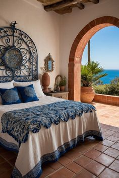 a bed with blue and white comforter next to an arched window overlooking the ocean