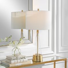 a table with a lamp, mirror and flowers on it in front of a white wall