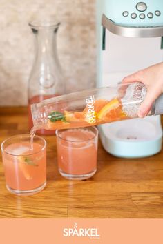 a person pouring orange juice into two glasses next to a blender on a wooden table