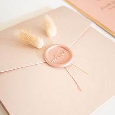 a pink envelope with a wax stamp and some white feathers