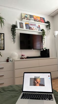 an open laptop computer sitting on top of a bed next to a wall mounted tv