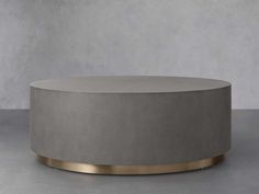 a round concrete coffee table with gold trim around the top and bottom, in front of a gray wall