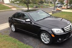 a black mercedes c class parked on the side of the road in front of a house