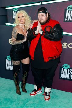 two people standing on a blue carpet with one person wearing a red and black jacket