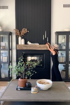 a woman standing in front of a fireplace with a bowl of food on the table