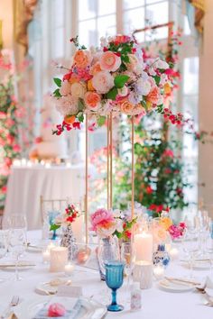 a tall vase filled with lots of flowers on top of a table next to candles