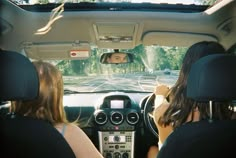 two women sitting in the driver's seat of a car looking at an intersection